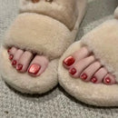 Beige slippers worn with toes showing and red nail polish on a neutral background, Obroi