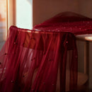 Red sheer fabric with beads draped over a chair in a softly lit room, Obroi
