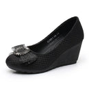 A single women's black wedge pump shoe with a textured woven upper and a decorative black mesh bow embellished with silver rhinestones on the toe, shown against a plain white background, Obroi