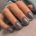 Close-up of a hand with glittery silver nail polish on a textured surface, Obroi