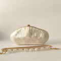 Silver clutch bag with a gold chain on a light beige background, Obroi