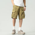 A person wearing olive green cargo shorts with side drawstrings, a white t-shirt, white socks, and beige hiking shoes, shown from the waist down against a light gray studio background, Obroi