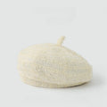 A textured cream-colored bouclé beret hat with a short top loop, photographed on a seamless light gray background, Obroi