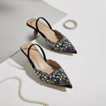 Pair of black embellished shoes on a light gray background with a pearl necklace, Obroi