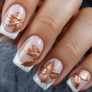 Nails with white polish and copper leaf designs on a textured surface, Obroi
