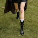 Person wearing black rain boots and a black coat on grass with fallen leaves, Obroi