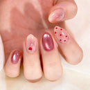 Close-up of a hand with pink nail polish and heart designs on a light background, Obroi