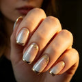 A close-up of a hand with French manicure nails featuring a glossy white-to-gold gradient and fine gold glitter, Obroi