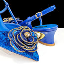 Blue sequined high-heeled sandals with a large decorative flower embellishment on the toe area, shown on a white surface against a black background, Obroi