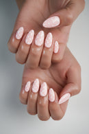 Close-up of a hand with pink nail polish and white polka dots on a neutral background, Obroi