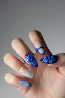 Hand with blue floral nail art on a neutral background, Obroi