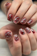 Close-up of a hand with red and silver nail art on a blurred background, Obroi