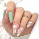 Hand with pastel green and pink nails featuring white floral designs on a white background, Obroi