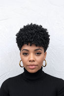 Woman with styled black hair wearing gold hoop earrings against a white background, Obroi