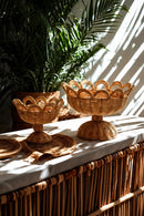 Two woven baskets on a table with plants in the background, Obroi