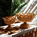 Two woven baskets on a table with plants in the background, Obroi