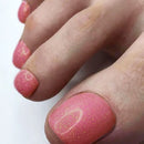 Close-up of toes with pink nail polish and gold glitter on a white background, Obroi