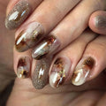 Close-up of a hand with decorative nail art featuring gold and brown elements, Obroi
