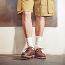 Person wearing brown shoes, white socks, and beige shorts against a neutral background, Obroi