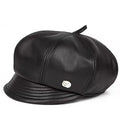 A black leather cap with a structured crown, stitched paneling, a short brim, and a small silver metal emblem on the side, shown against a plain white background, Obroi