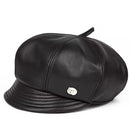 A black leather cap with a structured crown, stitched paneling, a short brim, and a small silver metal emblem on the side, shown against a plain white background, Obroi