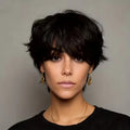 Woman with short black hair wearing gold earrings and a black top against a gray background, Obroi