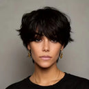 Woman with short black hair wearing gold earrings and a black top against a gray background, Obroi