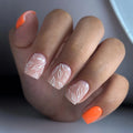 Hand with orange nail polish on one finger and leaf designs on the others against a neutral background, Obroi