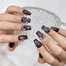 Close-up of hands with dark purple nail polish holding a glass container, Obroi