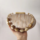 Hand holding a beige and brown marbled clutch bag with gold accents, Obroi