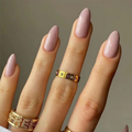 Close-up of a hand with pink nail polish and gold rings on a neutral background, Obroi