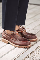 Brown leather shoes with tan soles worn by a person on a wooden floor, Obroi