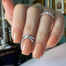 Hand with peach-colored nails and silver rings on a blurred indoor background, Obroi