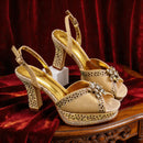 Gold high-heeled shoes with rhinestone embellishments on a red velvet background, Obroi