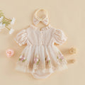 A baby girl's cream-colored waffle-knit romper with a matching bow headband, styled in a flat lay with decorative flowers and woven balls on a beige background, Obroi
