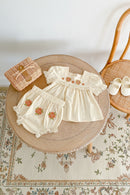 Children's white outfit with floral embroidery on a wooden surface, Obroi