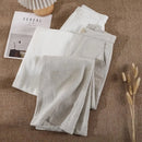 Folded beige pants on a textured surface with a magazine and decorative elements, Obroi