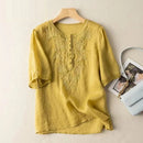 Yellow embroidered blouse on a hanger with a handbag and photo album in the background, Obroi