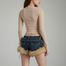 Person wearing a beige long-sleeve top and denim shorts with fur trim on a gray background, Obroi