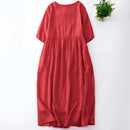 A red linen midi dress with short sleeves and a gathered waist, shown flat-laid on a white background with a small green plant in the top right corner, Obroi
