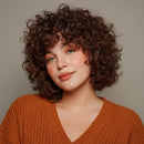 Woman with curly hair wearing an orange patterned top against a neutral background, Obroi