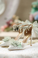 White heeled sandals with floral decorations and pearl embellishments on a blurred background, Obroi
