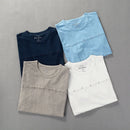 Four folded t-shirts in navy, light blue, gray, and white on a gray background, Obroi
