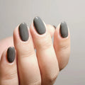 Close-up of a hand with dark gray nail polish on a neutral background, Obroi