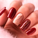 Close-up of a hand with red and gold nail art on a soft pink background, Obroi