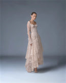 A model wearing a long-sleeved, tiered lace maxi dress in a light beige or cream color, standing against a neutral gray studio background, Obroi