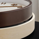 Close-up of a round wooden game board or tray with a dark brown outer ring, a light natural wood inner ring, and a white playing surface with small wooden pieces, Obroi