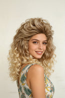 A woman wearing a voluminous, curly wig with a blonde ombre transition, photographed against a plain light background, Obroi