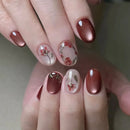 Close-up of a hand with maroon nail polish and floral designs on a neutral background, Obroi