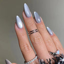 Hand with light gray nail polish and multiple rings on a neutral background, Obroi